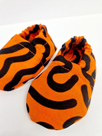 Orange baby crib shoes with a black squiggle